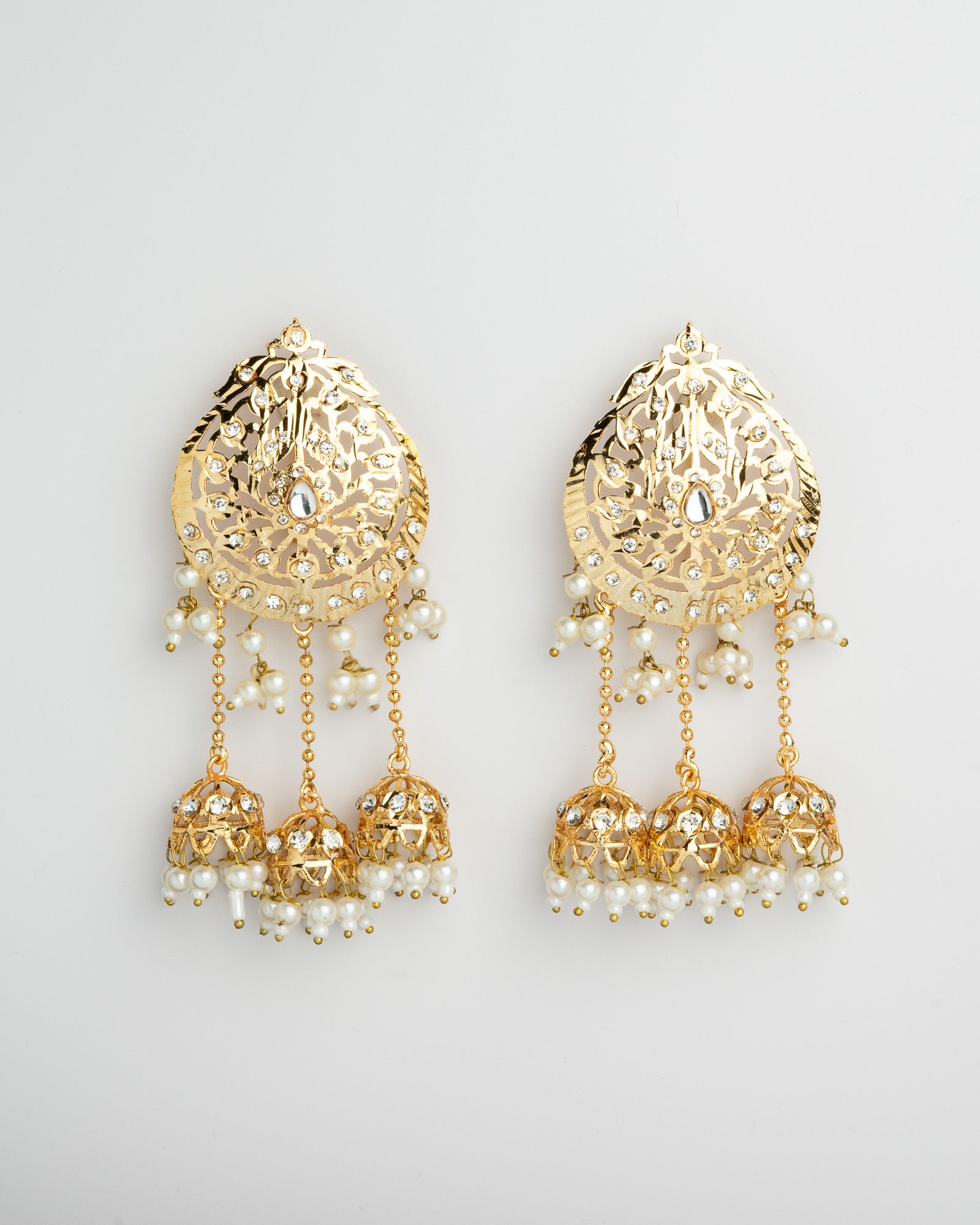 Golden earrings with intricate designs and pearl-like beads on a light gray background