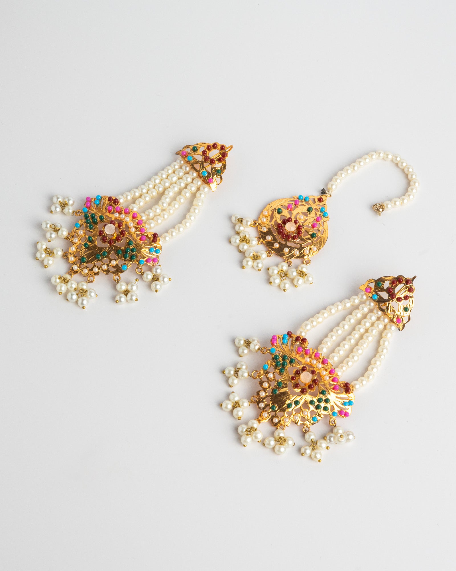 Golden and pearl earrings set with colorful embellishments on a light gray background