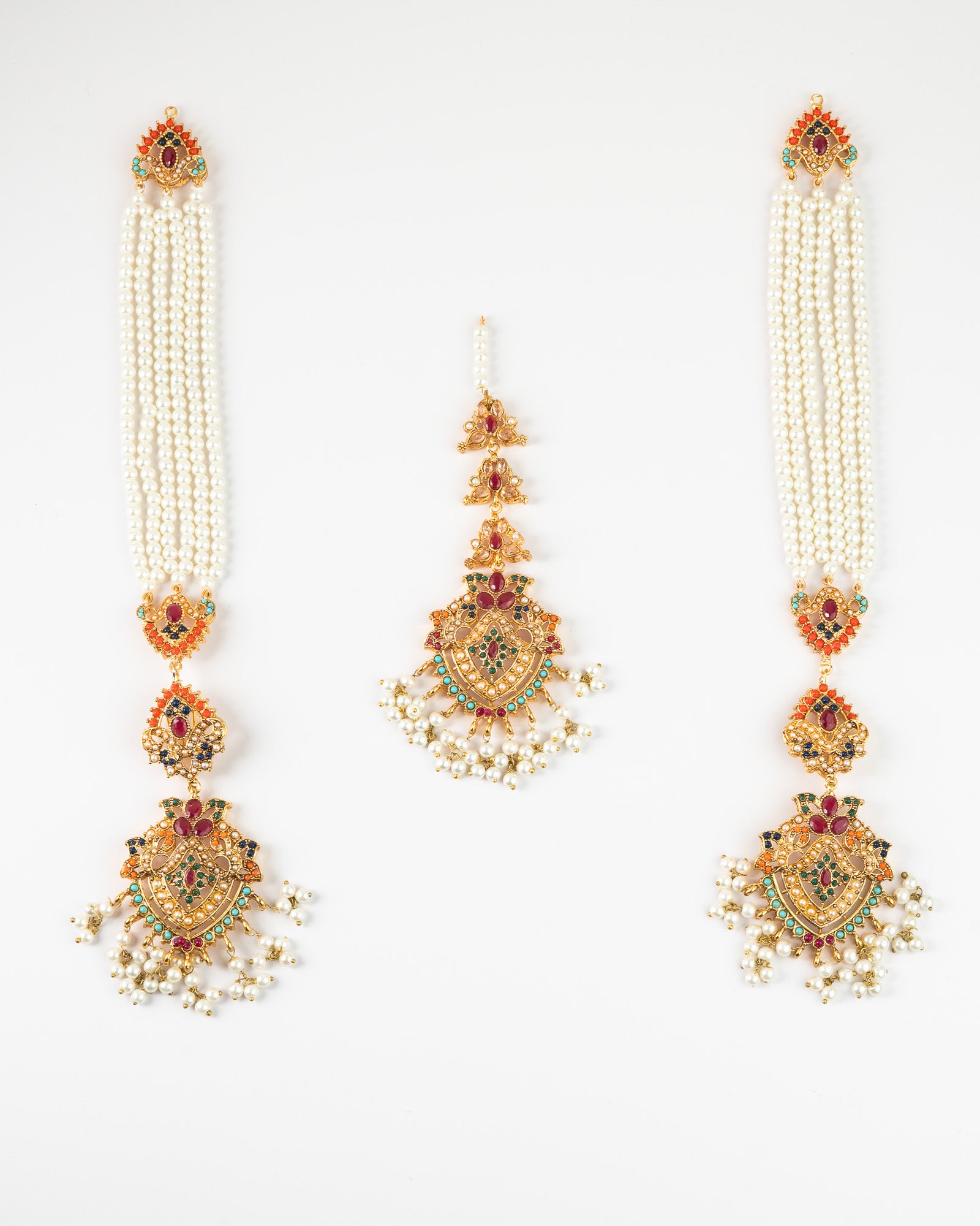 Pair of earrings and maang tikka with pearls and gemstones on a white background