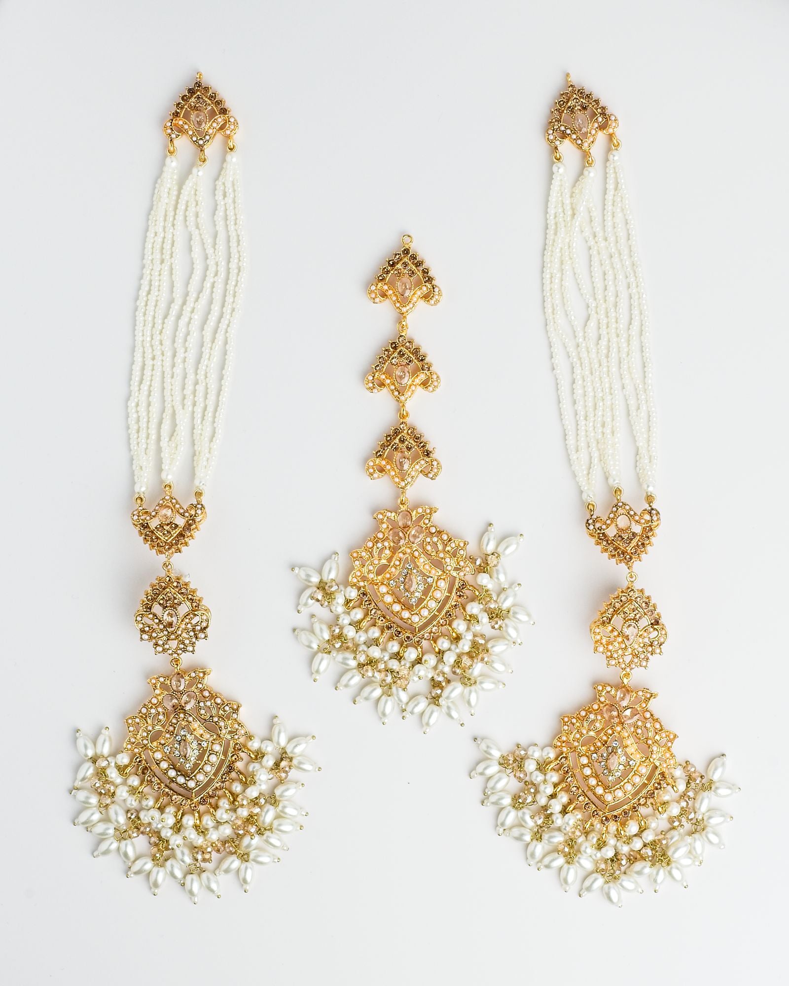 Pair of golden and pearl earrings with attached ear chains and a matching maang tikka on a white background