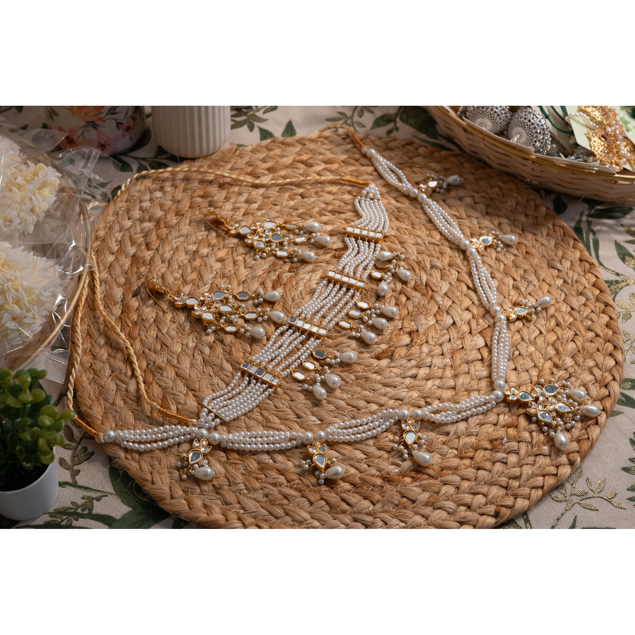 Pearl and kundan choker and long necklace with matching earrings on a woven mat with a floral table cloth background